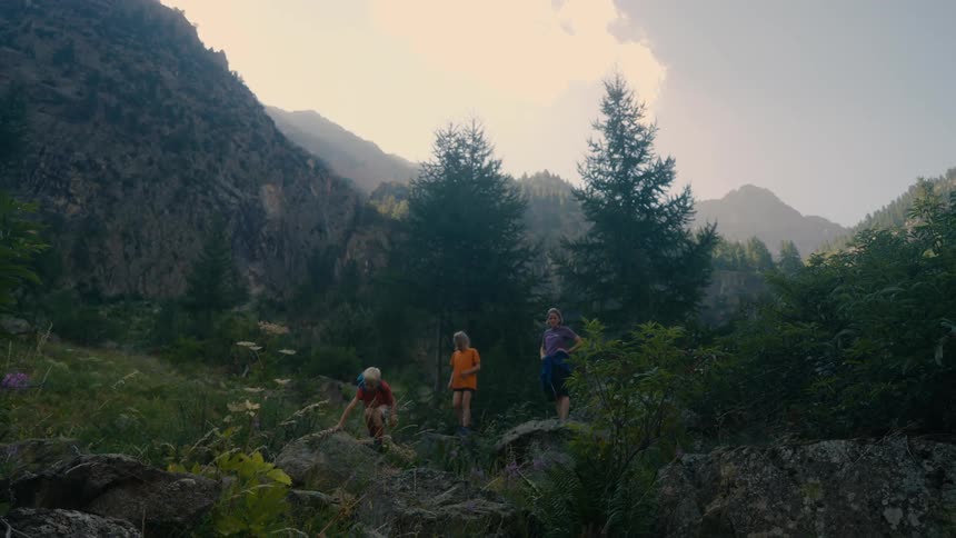 Two children accompanied by an adult jumping on rocks while hiking in the mountains