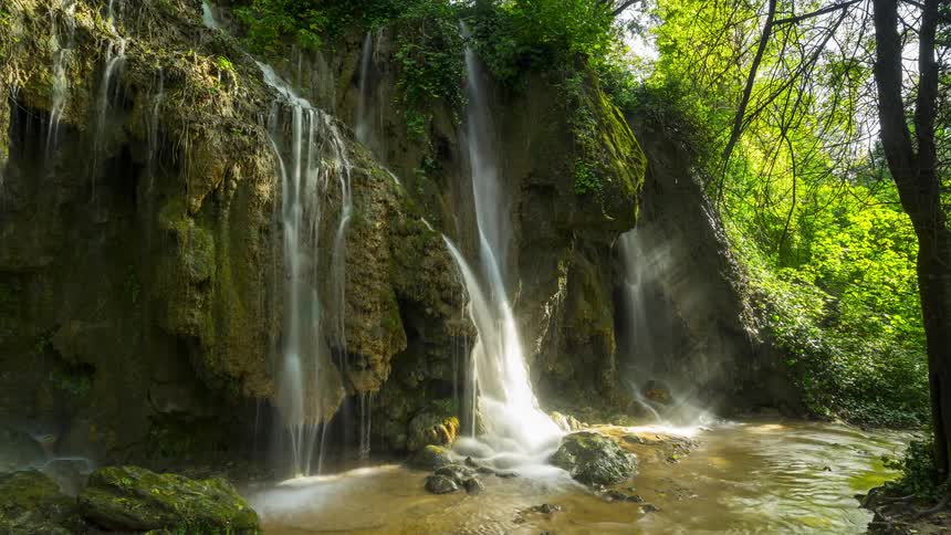 A small waterfall with water coming out of rocks in a forest and falling into a stream