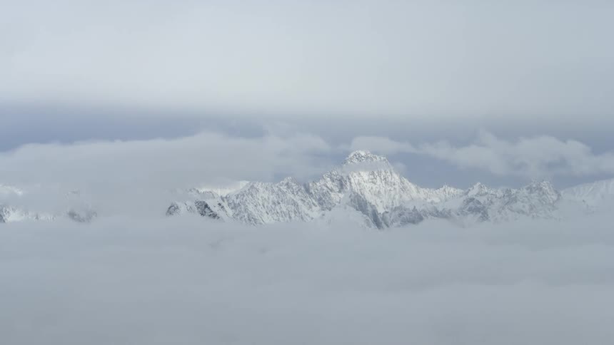 Clouds hover just below the peak of a tall mountain covered with snow