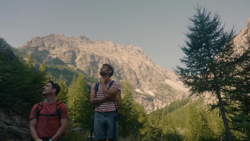 Two hikers stand looking up at a mountain vista likely taking in the scenery