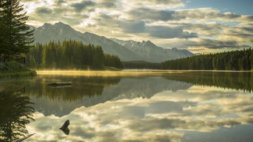 Natural landscape of a lake reflecting the conifers on the banks and mountains in the background