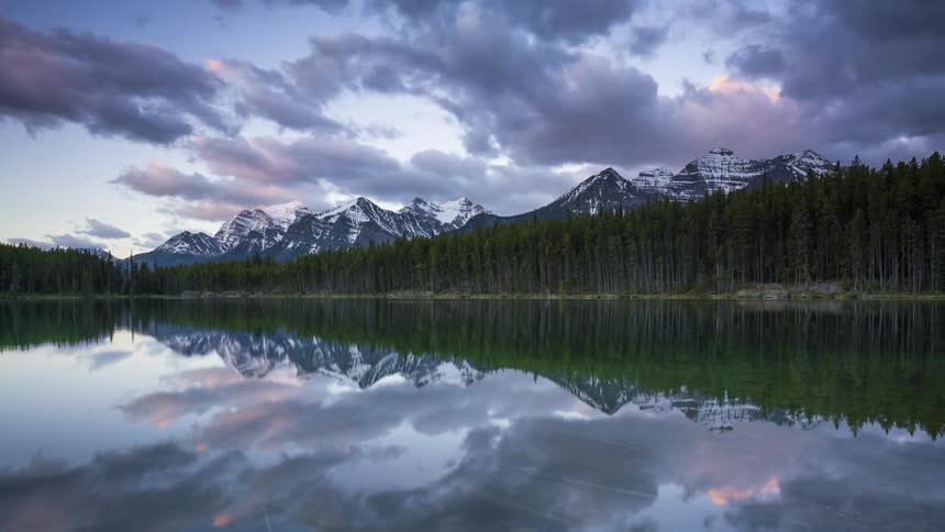 Lake waters reflect the forest and nearby mountains as night turns to day