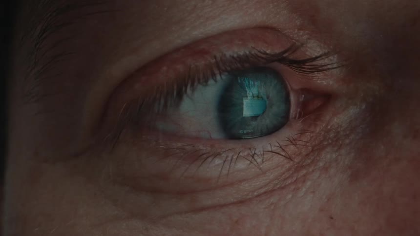 The green eye of a person who has a reflection of scrolling on social media in his iris