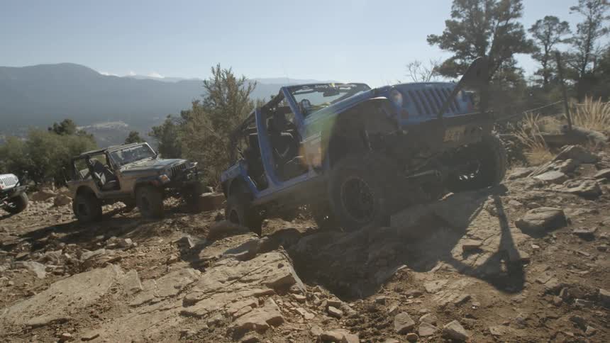 Three jeeps crawl slowly uphill over large rocks in the mountains