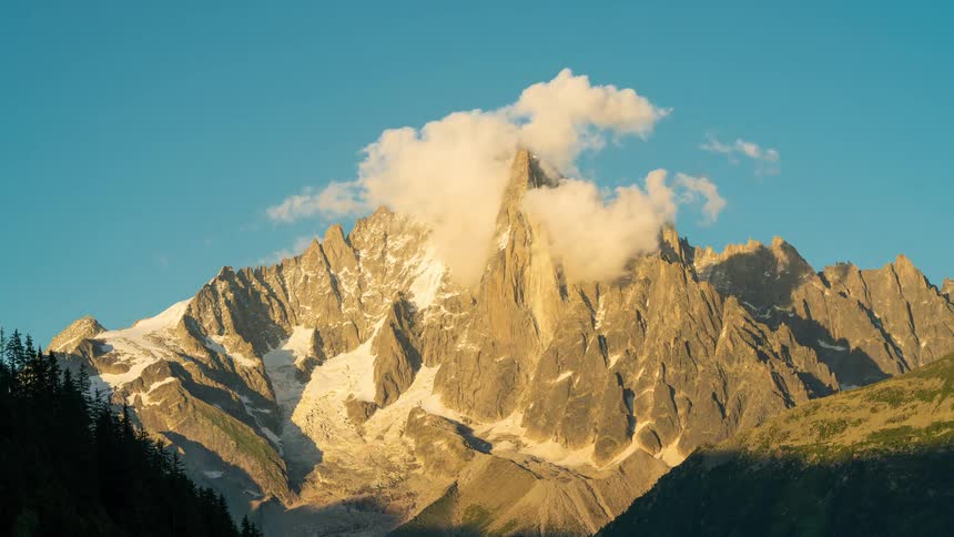 Clouds hover over a mountain peak on a clear summer day