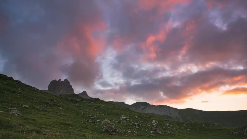 Dark storm clouds move over a mountain range and grassy area dotted with various sized stones