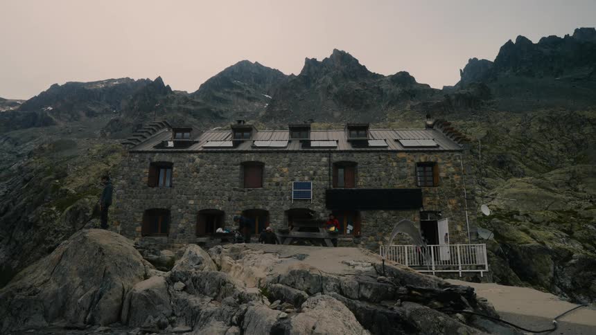 People move around outside an old stone house near a mountain range