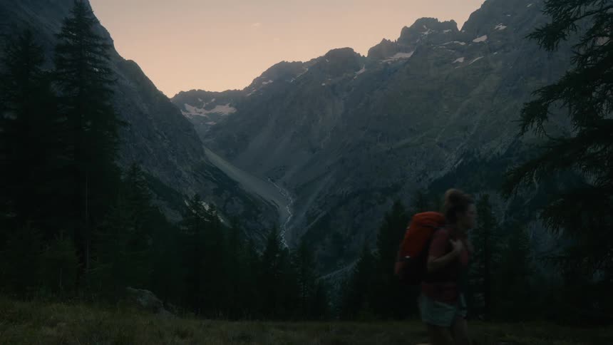 A lone hikers walks amidst a mountain valley with majestic peaks in the soft morning light