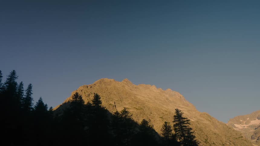A mountain peak partially shadowed by trees is shown against a pale blue sky