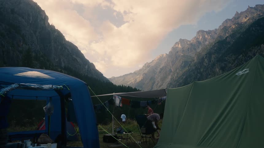 People hang clothes to dry on a makeshift clothesline between two tents with a majestic mountain range in the background