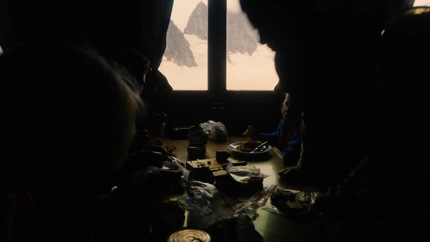Silhouette of a family enjoying a meal in a dimly lit room next to a window overlooking a snowy mountain peak