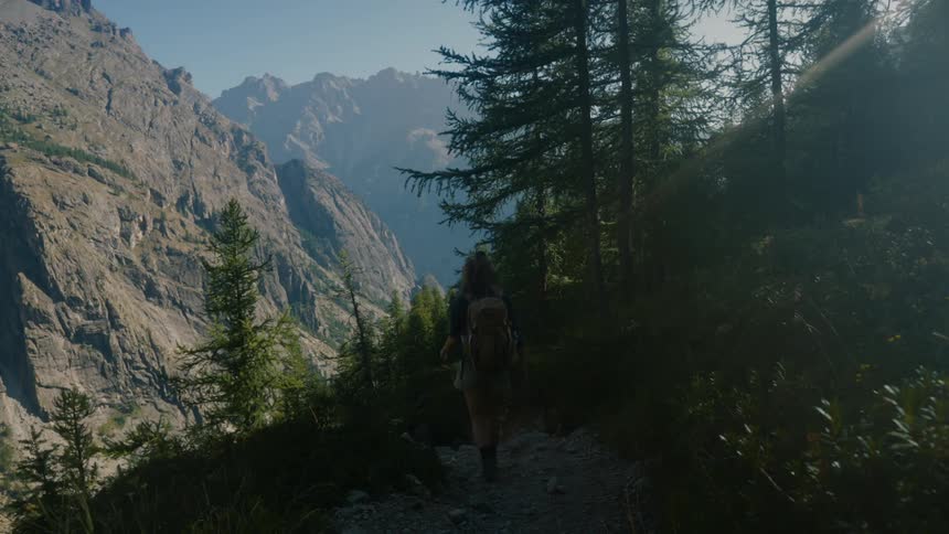 A person hiking down a mountain trail with a mountain range visible in the background