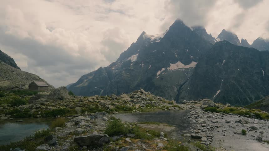 A mountainous region with a snowy peak in front of a rocky peak with some puddles of water