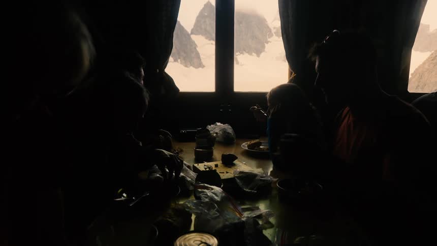 Silhouette of a family enjoying a meal in a dimly lit room with a window showing a snowy mountain peak