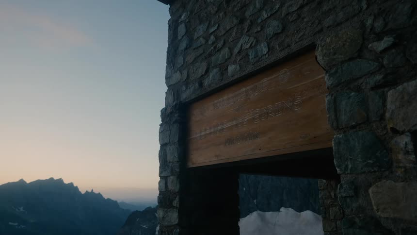 Close up of a wooden sign embedded on a stone building overlooking a mountainside