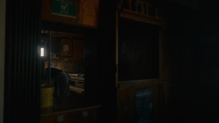 A person is seen working in a dimly lit interior space partially visible through a doorway with various items on shelves and walls