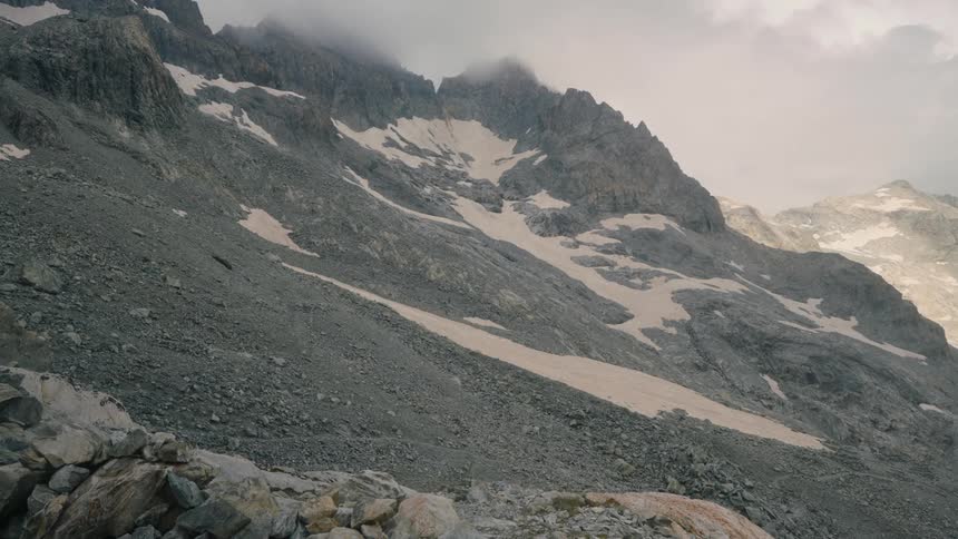 A gray mountain pass dotted with snow on a foggy cloudy day