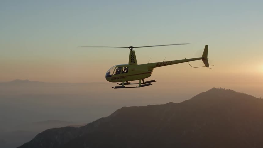 Helicopter flying above the mountains with the sun setting in the distance