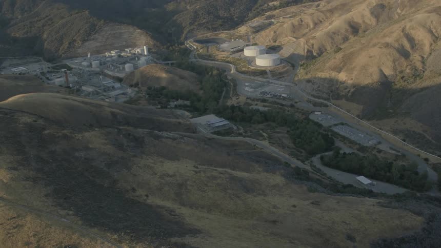 Industrial tanks and buildings sit in a barren valley during the day