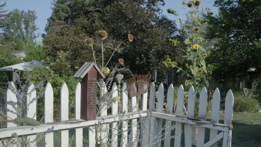 A birdhouse is sitting on a fence in a yard