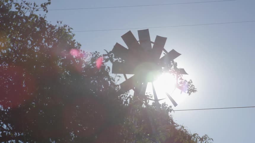 Sun shining through a spinning windmill on a clear day