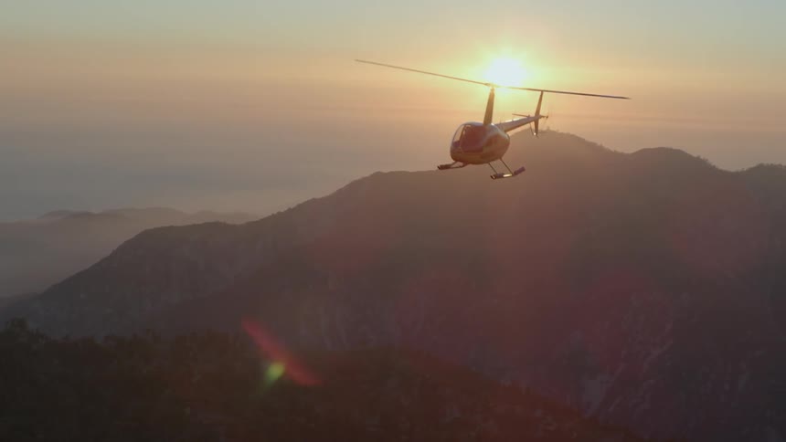 Helicopter flying as the sun sets in the background as seen from another helicopter
