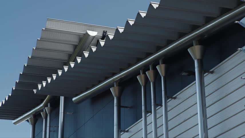 A modern architectural detail with a unique angular roofline and a series of vertical cylindrical supports creating a striking visual pattern