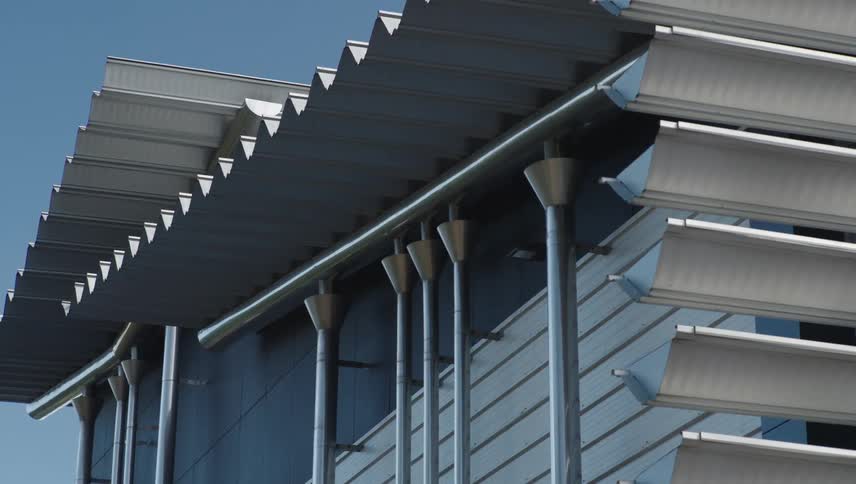 Metal columns line a metallic building with an elaborate architecture under a blue sky