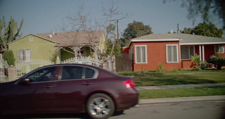 A car drives past a row of houses with a cactus and trees in the foreground