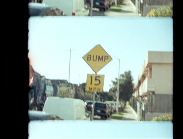 Garbage truck about to pass a sign providing notice of a street bump moves by several parked cars