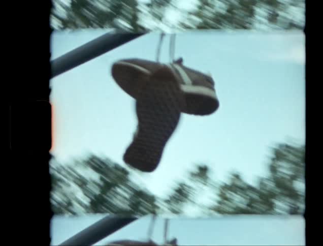 A pair of sneakers hangs from a metal bar against a blue sky