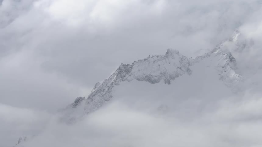 Snow-covered caps of mountains as seen amongst the clouds