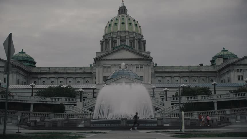 Runner passes a fountain before the small group conversing in front of a large building