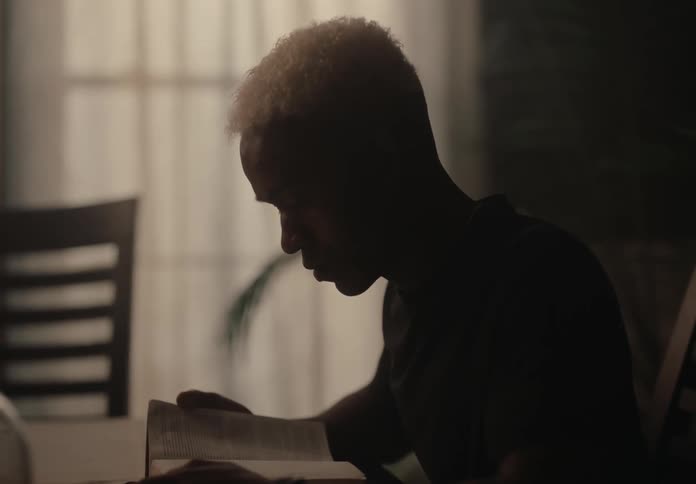 Man wearing a black sweater sits reading a book at night