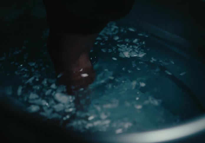 A person getting into a bathtub filled with water with a little ice on the surface