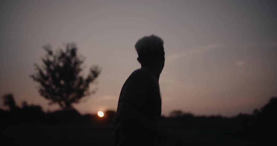 Man running in the field is silhouetted against the sunset