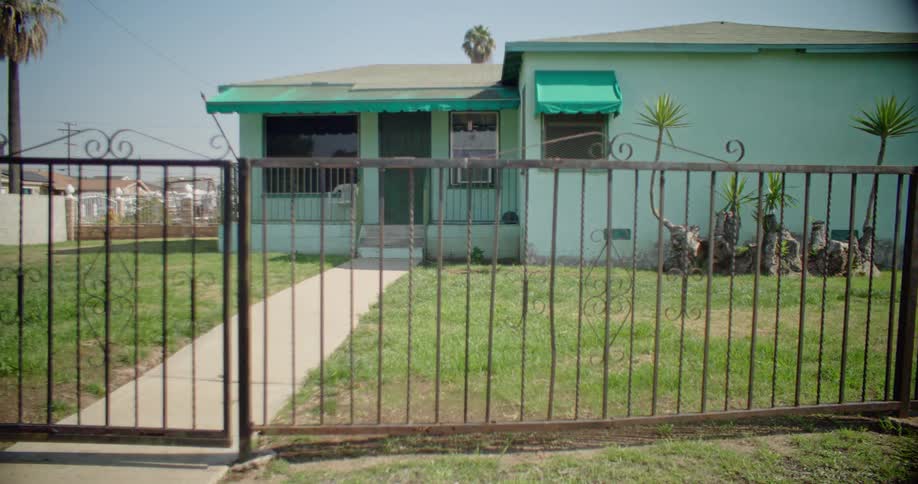 A blue house with a porch and a metal fence in front of it
