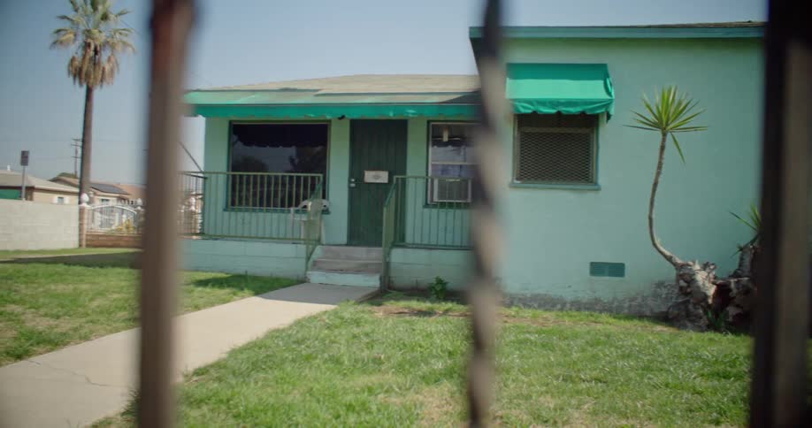A blue house with a porch and a metal fence in front of it