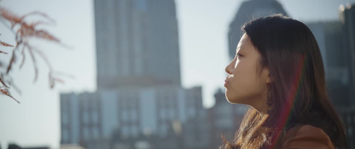 Woman stares into distance with buildings in the background on a cloudy day