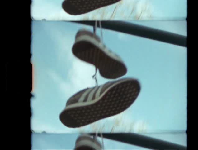 A pair of sneakers hangs from a metal bar against a blue sky