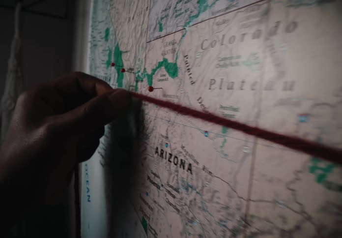 A hand traces a route with a thread on a map hanging from a wall