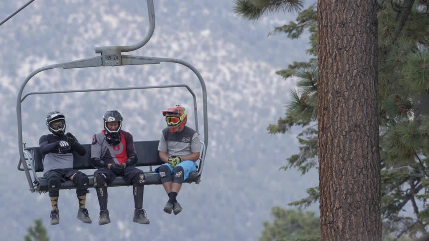 Three people wearing helmets are riding up a ski lift