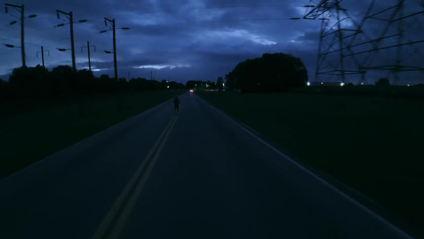A man runs along a highway past utility poles and trees on a cloudy night