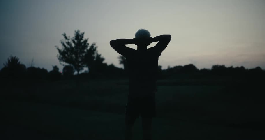 A man is stretching on the field at sunrise