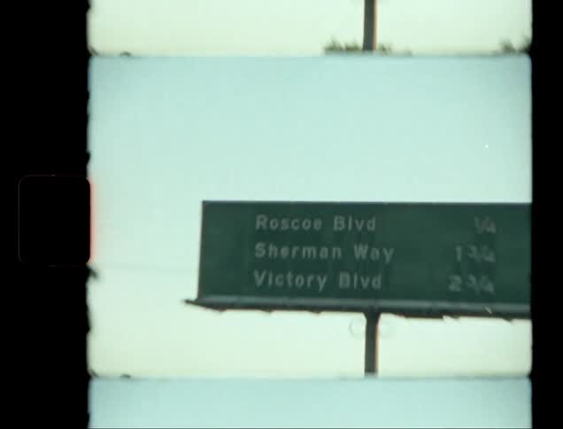 A large green traffic sign with white writing on a busy highway