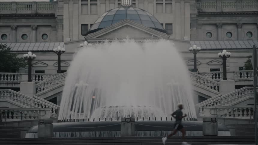A man runs past a large fountain in front of a grand building