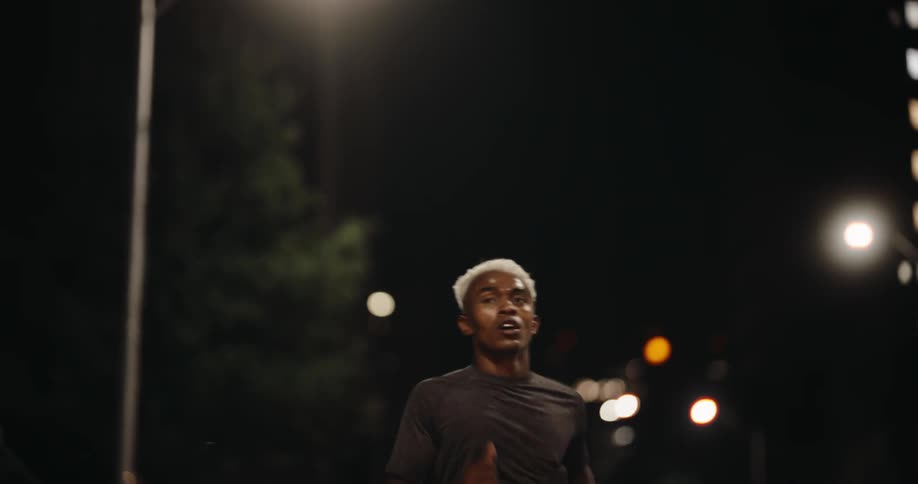 A young man is running down a street at night and he is sweating