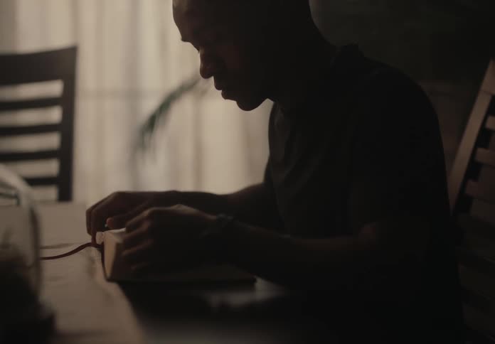 A man stands in a partially dark room while leafing through a book and reading it