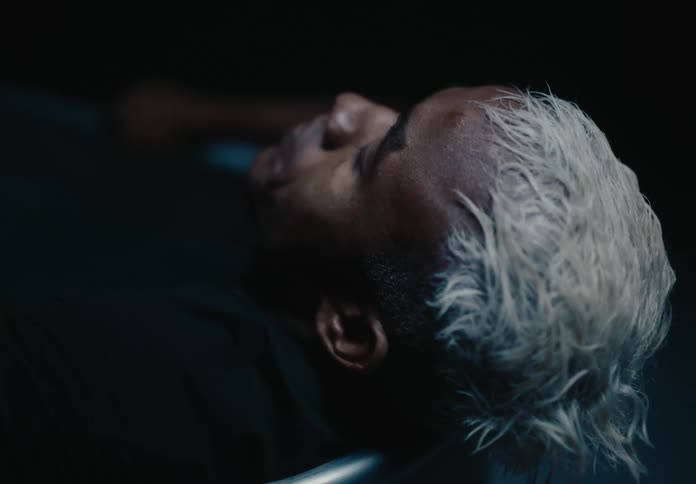 A man with white hair is lying in a bathtub and he is shaking from the cold while making expressions with his face and his eyes are closed