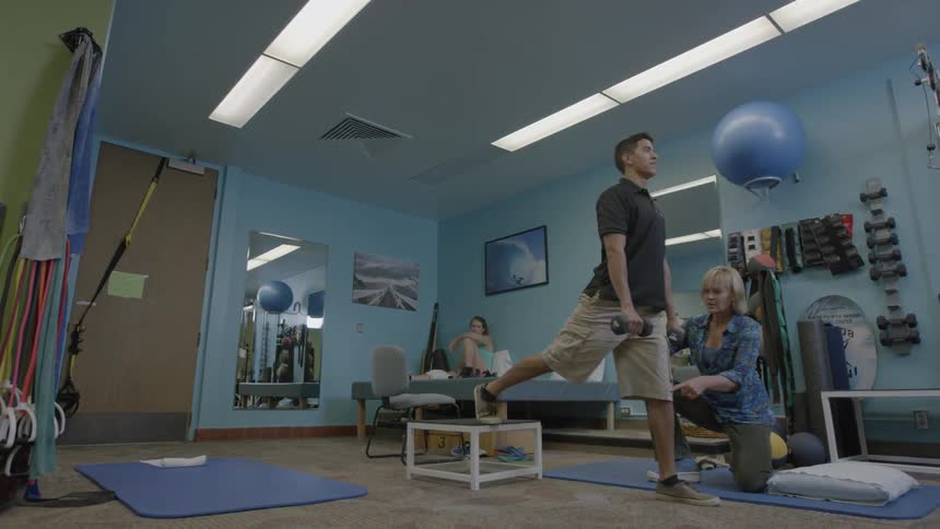 Man exercising in what looks like a rehabilitation with the aid  of someone helping him